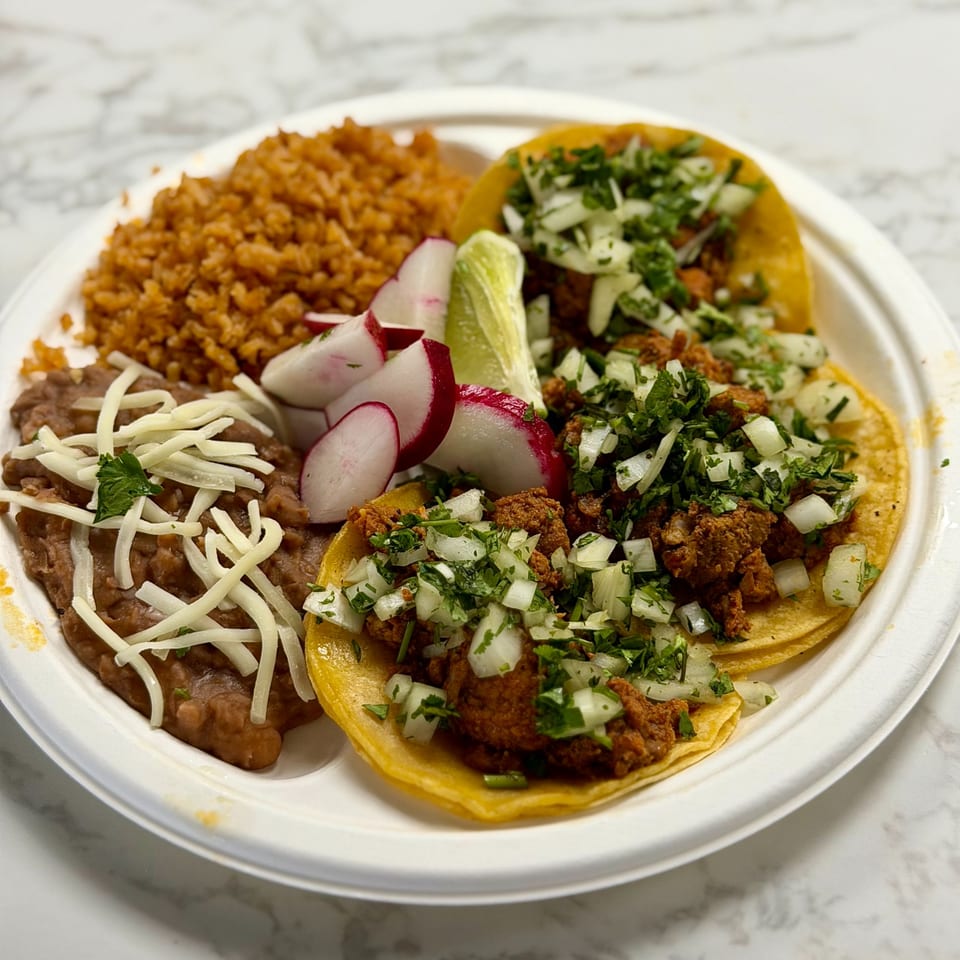 Three Studio Tacos with rice, beans, radishes, and lime on a white plate.