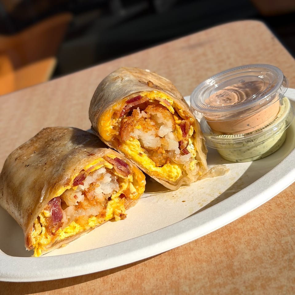 Two halves of a Studio Tacos breakfast burrito with bacon, egg, and hash browns, with two sauces.