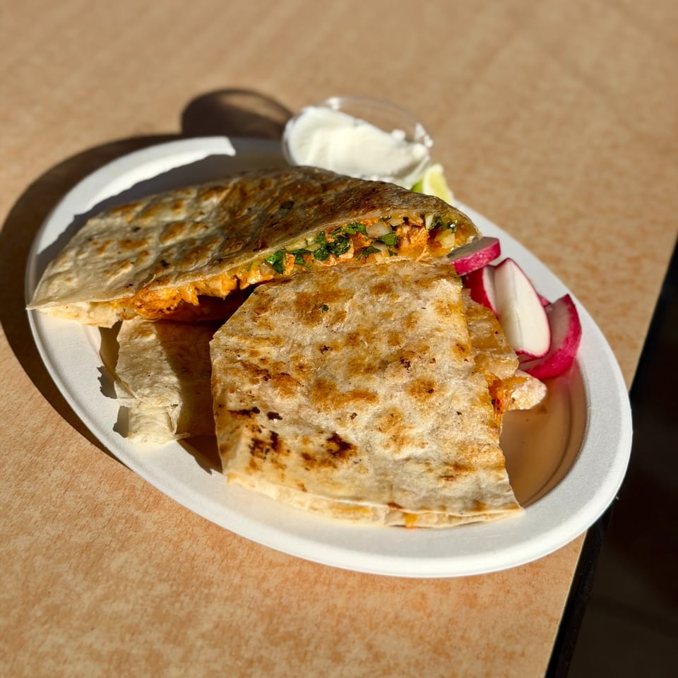 A Studio Tacos quesadilla with chicken, onions, and cilantro, served with radishes and sour cream.