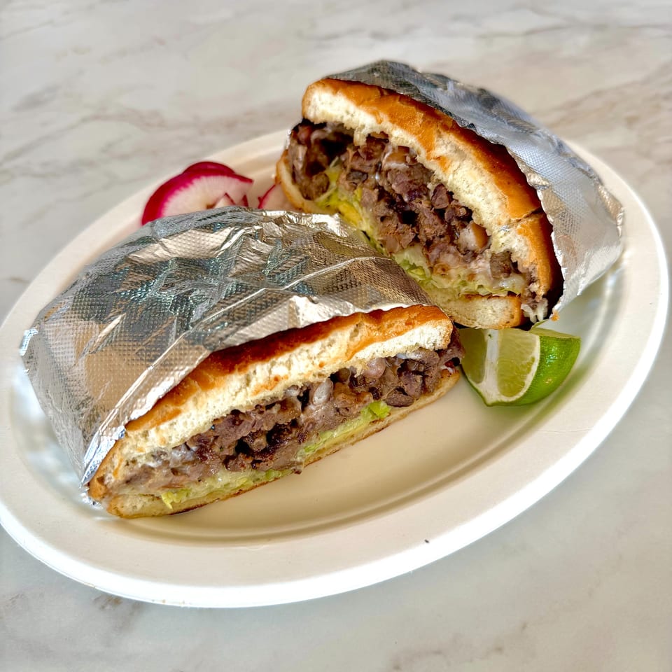 A Studio Tacos Mexican torta, cut in half, wrapped in foil, with lime and radish.